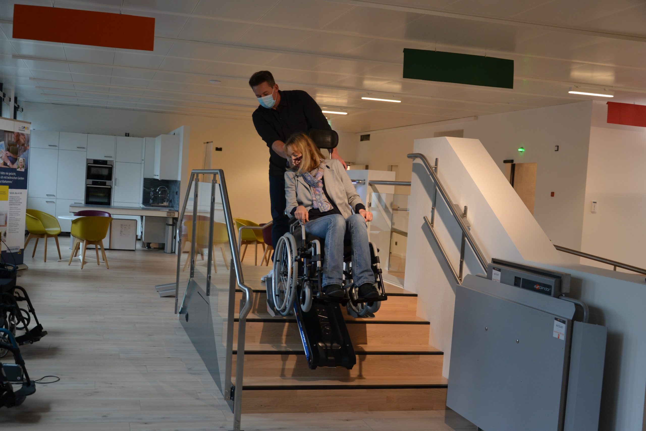 Ein Mann zieht einen Rollstuhl, in dem eine Frau sitzt, die Treppen hoch.