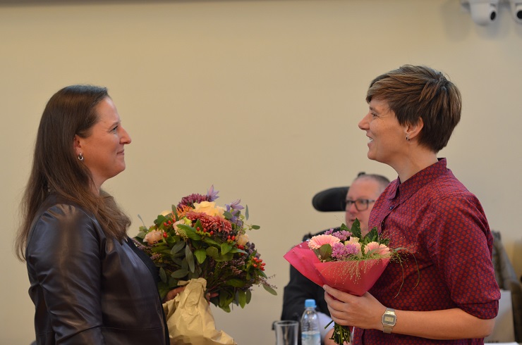 Zwei Frauen mit Blumensträußen sehen sich freundlich an.